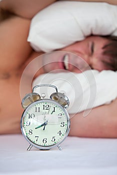 Angry man in bed annoyed by his alarm clock
