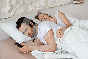 Angry man checking his sleeping girlfriend& x27;s smartphone, lying in bed at home, husband feeling jealous