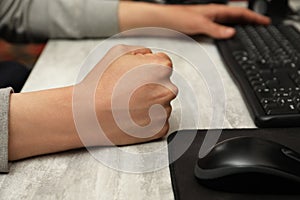 Angry man with clenched fist working on computer at table, closeup