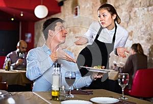 Angry man complaining to apologetic waitress about food in restaurant