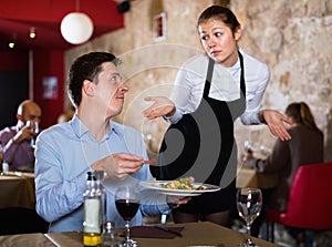 Angry man complaining to apologetic waitress about food in restaurant