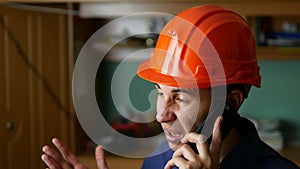 Angry man construction worker in a hardhat shouting, talking on the phone smartphone