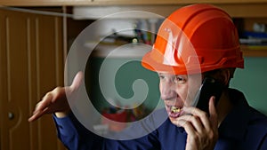 Angry man construction worker in a hardhat shouting, talking on phone smartphone