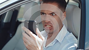 Angry Man Driver Using Smartphone while sitting in a car. Businessman is angry with the message that he read smartphone.