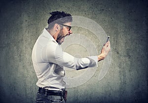 Angry man holding smartphone and shouting in anger