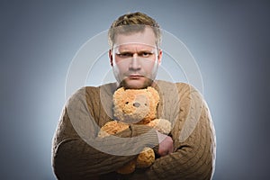 Angry man is holding a teddy bear and smiling on gray background