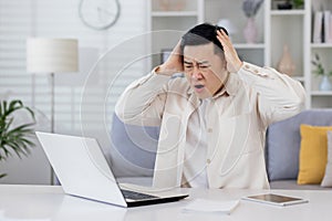 Angry man at home working with laptop frustrated asian man looking at laptop screen got bad news and unsatisfactory work