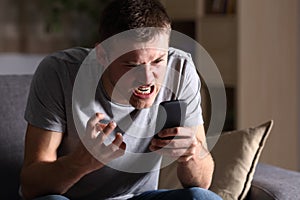 Angry man with a mobile phone at home photo