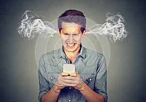 Angry man reading a text message on smartphone blowing steam coming out of ears