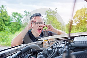 Angry man sitting beside a broken car calling for assistance