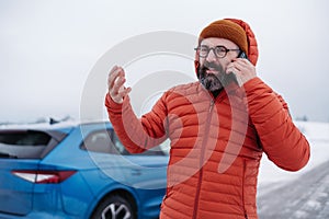 Angry man standing by electric car, battery run out of power before reaching destination. Man phone calling for help