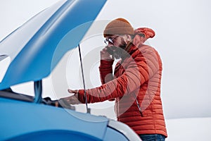 Angry man standing by electric car, battery run out of power before reaching destination. Man phone calling for help