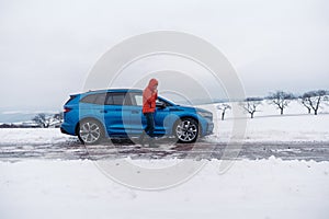 Angry man standing by electric car, battery run out of power before reaching destination, during snowy winter day