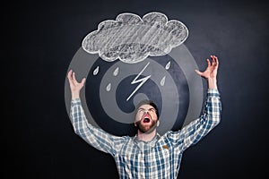 Angry man standing and shouting over blackboard with drawn raincloud