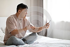 Angry mature asian man sitting on bed, have video chat