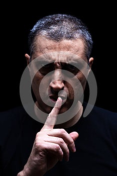 Angry mature man with an aggressive look making the silence sign in a threatening and creepy way.