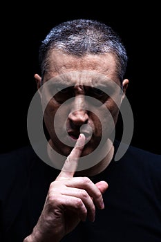 Angry mature man with an aggressive look making the silence sign in a threatening and creepy way. photo