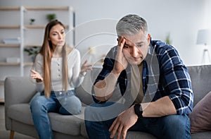 Angry mature woman shouting at her upset husband, having conflict at home, copy space