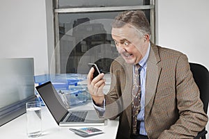 Angry middle-aged businessman looking at cell phone in office