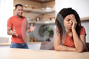 Angry millennial african american husband yelling at upset offended wife in kitchen interior, blurred