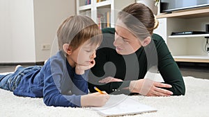 Angry mother scolding and talking to her silly son doing homework on floor in living room. Concept of domestic education