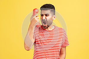 Angry nervous bearded man in striped t-shirt screaming and yelling talking retro landline phone, complaining on connection quality