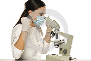 Angry nervous female scientist with protective face mask looking through a microscope