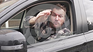 An angry, nervous male driver swears and punches the steering wheel in a car with the window open.
