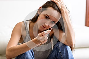 Angry and offended wife depressed after divorce, holding with hand a wedding ring sitting on a room floor.