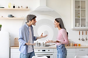 Angry offended young wife and husband shout, swear in kitchen interior. Couple arguing and conflicting