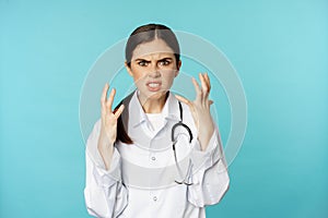 Angry and outraged woman shaking hands, cursing and looking furious, standing annoyed against torquoise background