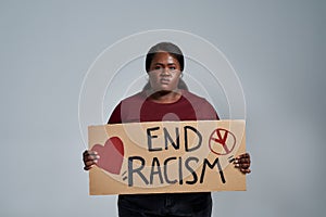 Angry plus size young african american woman in casual clothes looking at camera, holding End Racism banner in front of