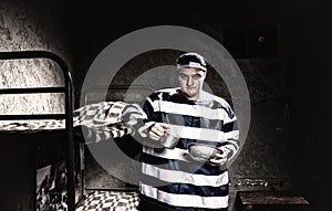 Angry prisoner wearing prison uniform holding aluminum dishes in