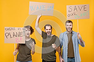 Angry protesting young three people hold protest signs broadsheet placard point on camera scream isolated on yellow