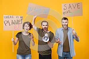 Angry protesting young three people hold protest signs broadsheet placard scream in megaphone isolated on yellow