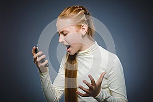 Angry redhead girl with cell phone. isolated on gray