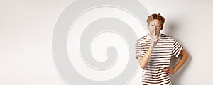 Angry redhead man looking displeased and hushing at camera, making shh gesture, standing over white background