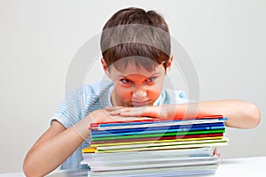 Angry schoolboy sitting at desk with pile of school books and notebooks photo