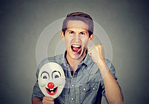 Angry screaming man holding clown mask expressing cheerfulness