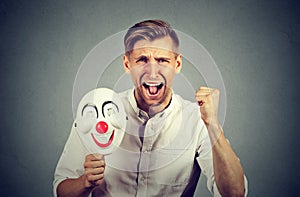 Angry screaming man holding clown mask expressing cheerfulness happiness