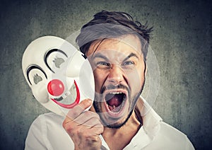 Angry screaming man taking off a clown mask