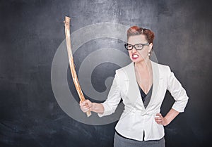 Angry screaming teacher with wooden stick on blackboard background