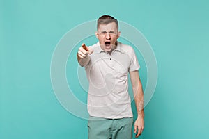 Angry screaming young man in casual clothes pointing index finger on camera, swearing isolated on blue turquoise