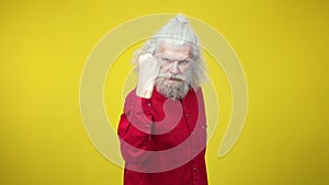 Angry senior bearded man threatening camera with clenched fist. Portrait of serious Caucasian retiree posing at yellow