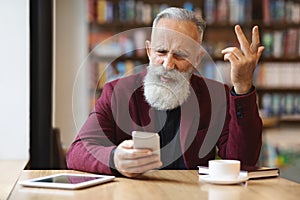 Angry senior man using mobile phone at cafe