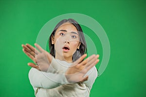 Angry serious asian woman showing gesture with crossed arms and looking at camera while standing isolated over green
