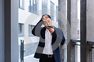 Angry and serious Successful Asian businessman explains information to employees using phone, speaks near office outside