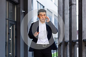 Angry and serious Successful Asian businessman explains information to employees using phone, speaks near office outside