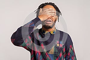 Angry shocked african guy with beard and dreadlocks closing eyes with hand, hiding, dont want to see and know, ignorance