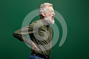 Angry shouting old man suffering from back pain isolated on green background